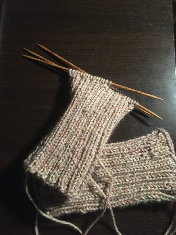 A pair of knit wristers (one done, one in progress and on the needles) in a pale khaki yarn.