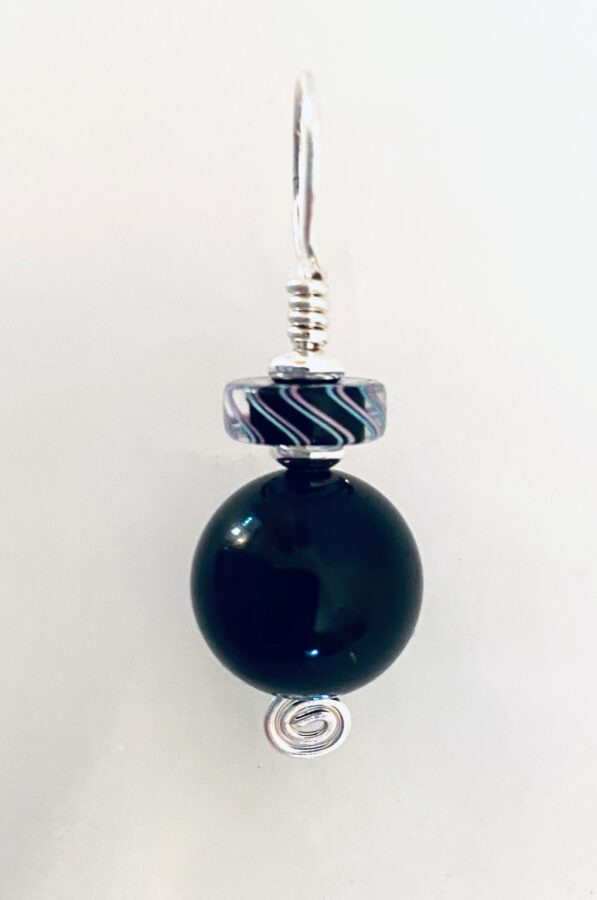 An elegant almost monochromatic pendant sharply contrasts against the plain white background. Silver wire is wrapped to form the pendant's head, with a spiral at the bottom. A disc with a black centre and tracing curves of pale blue and pink is mounted above a larger round black bead that gleams in the light.