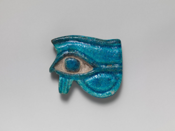A bright and glowing faience wedjat, showing the left eye of horus, surrounded by faience stylised lines that form the eyebrow, eye, and lashes. The blue pupil is set in inset unglazed ceramic, making a striking contrast. 